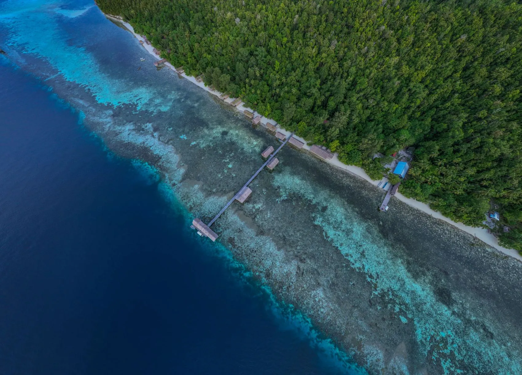 Aerial view of Kri Eco Resort's over-water cottages along a turquoise reef edge in Raja Ampat