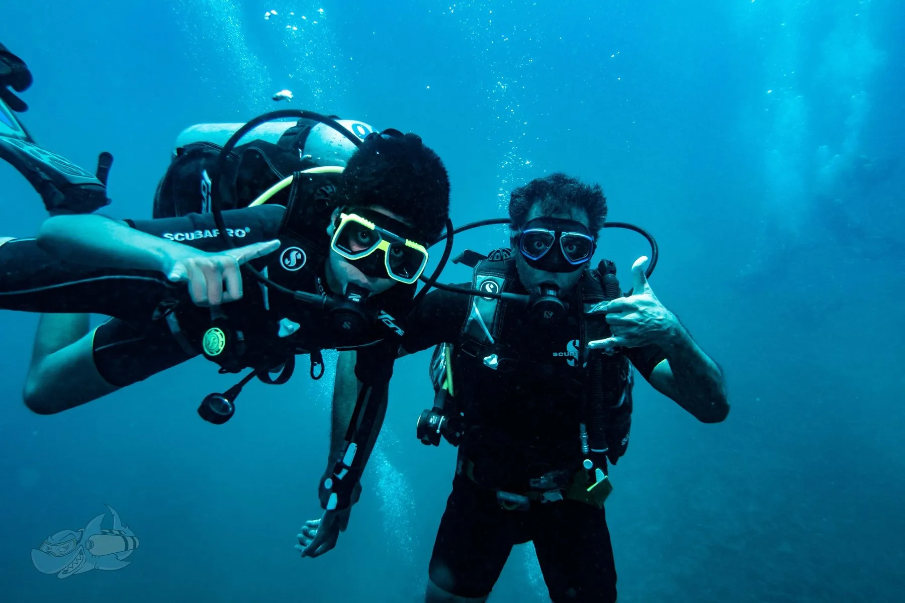 Buddy pair of divers side by side in blue water, facing the camera and signalling
