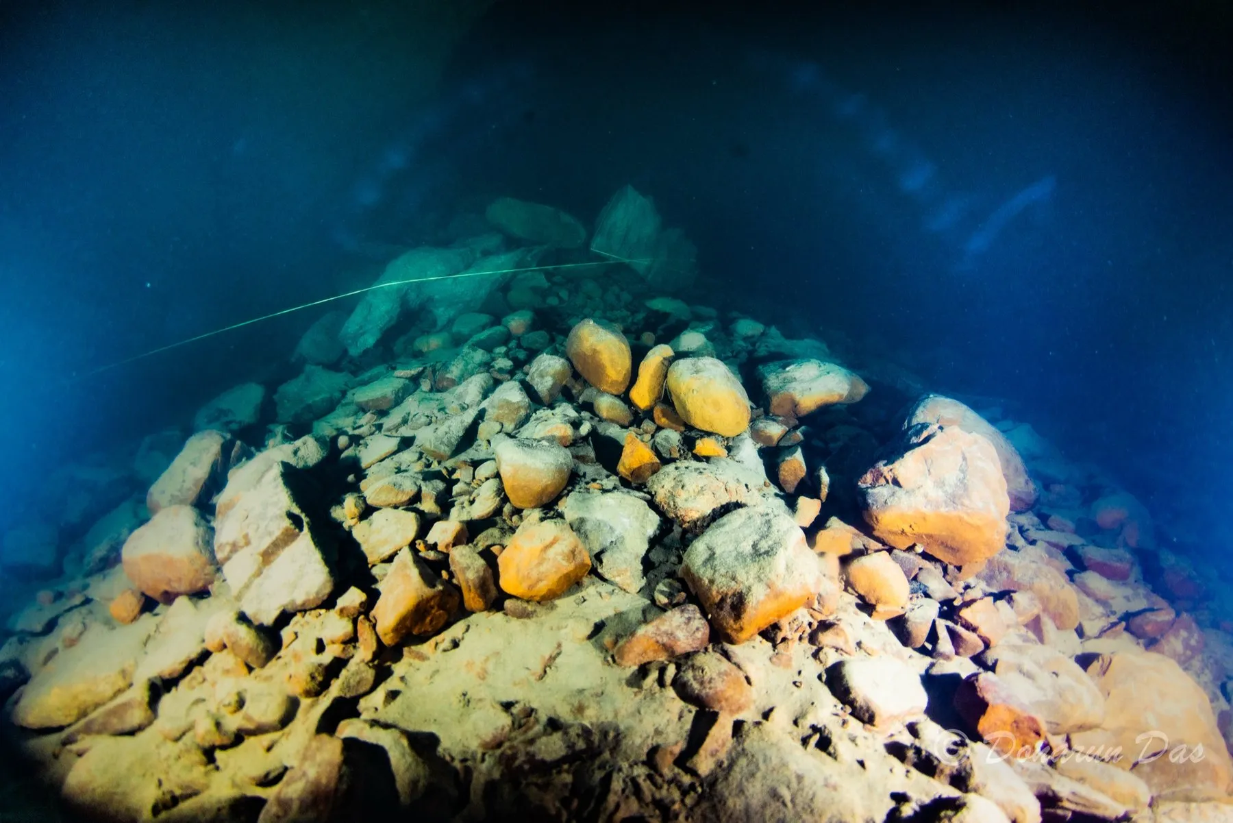 Thin guideline strung across a boulder-and-cobble slope in clear blue-green cave water