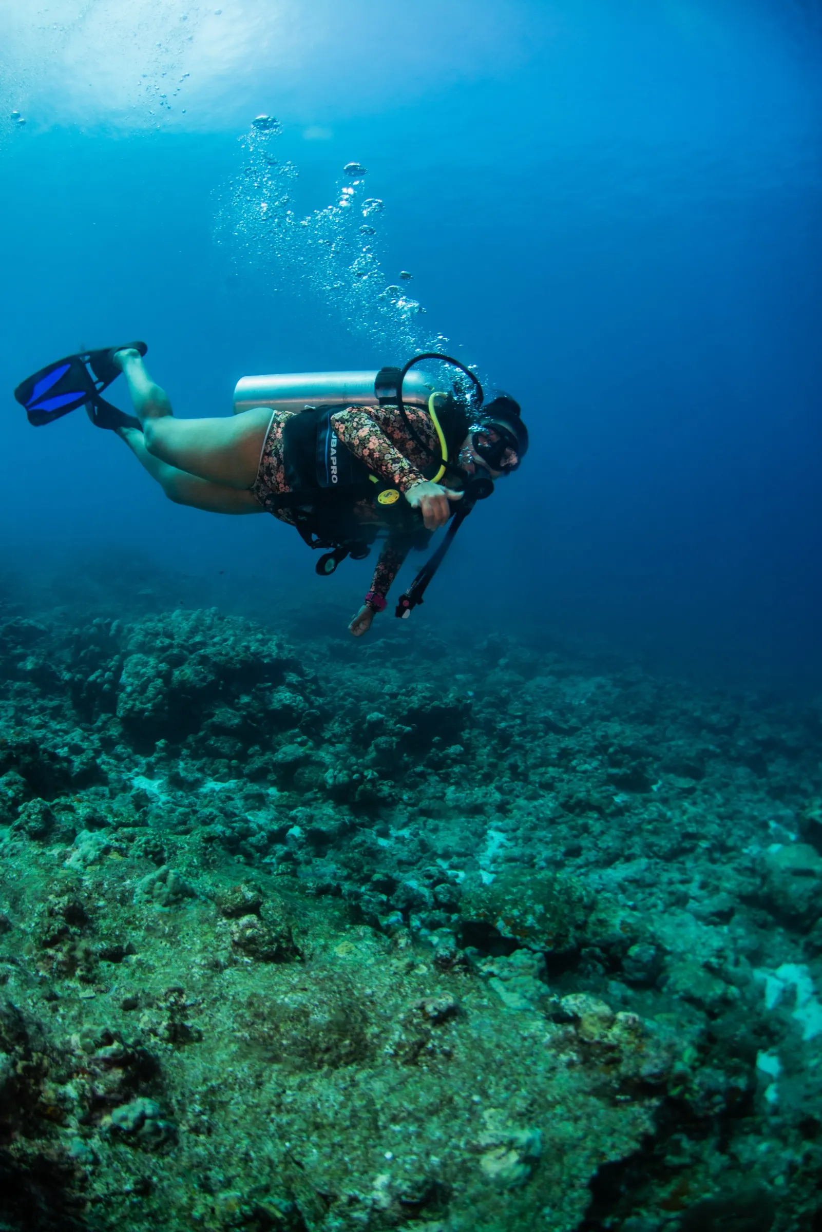 Diver in flat horizontal trim above a coral reef, fins raised and body level, exhaling bubbles
