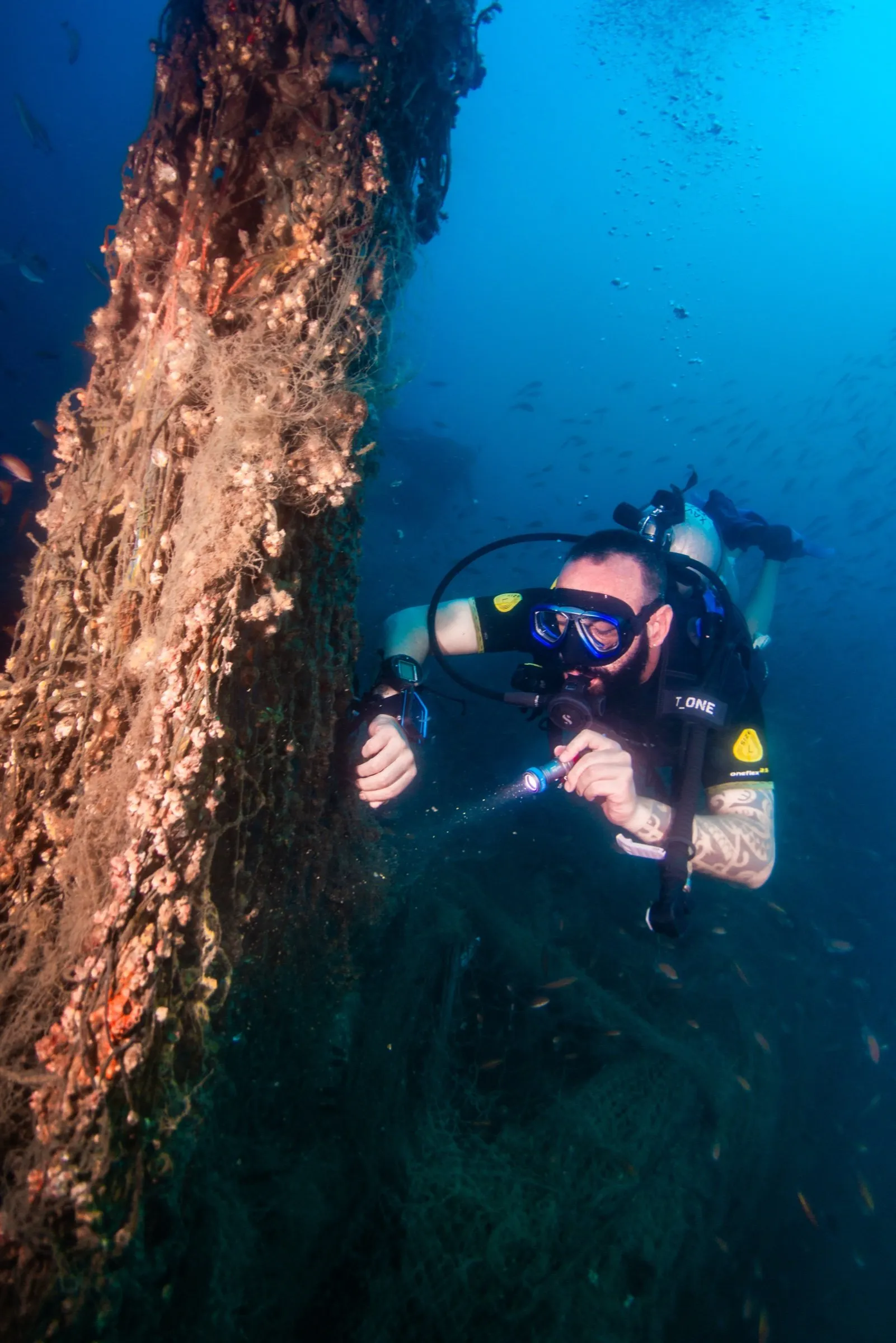Student diver lighting a heavily encrusted wreck hull with a primary torch