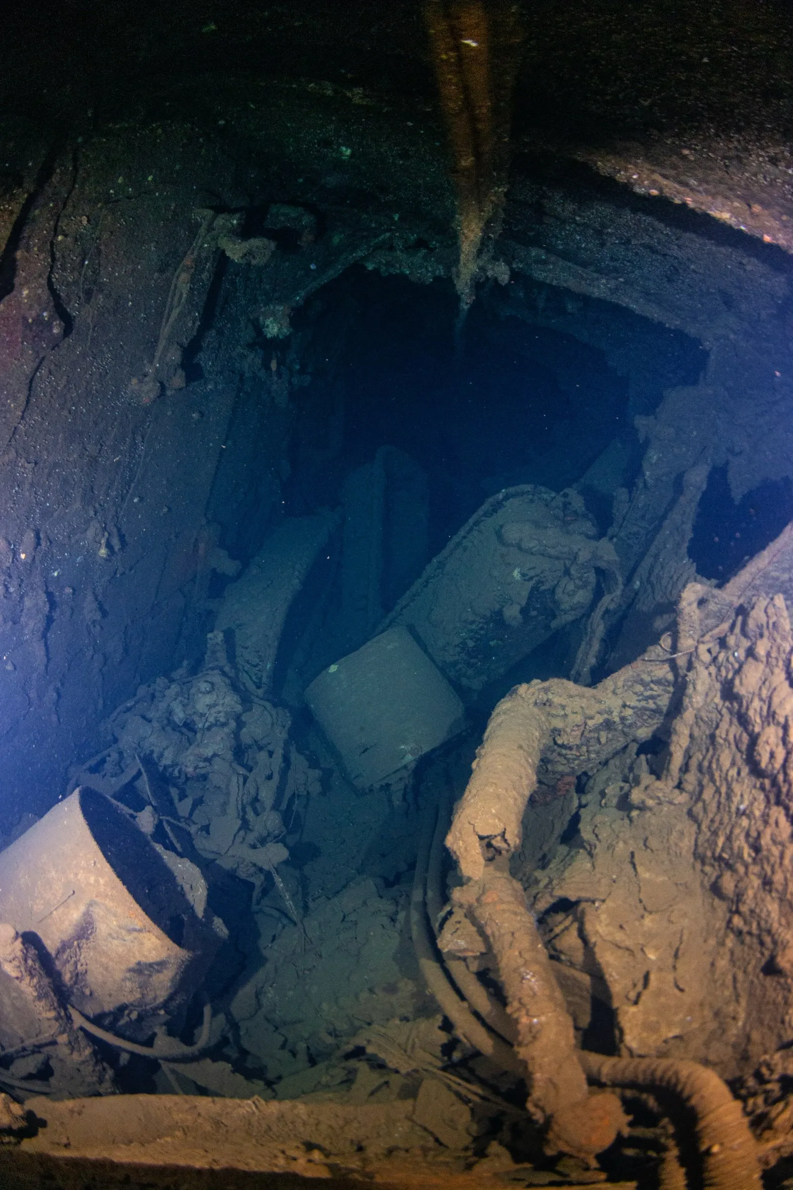 Debris and pipework in a dark lower hold of a wreck