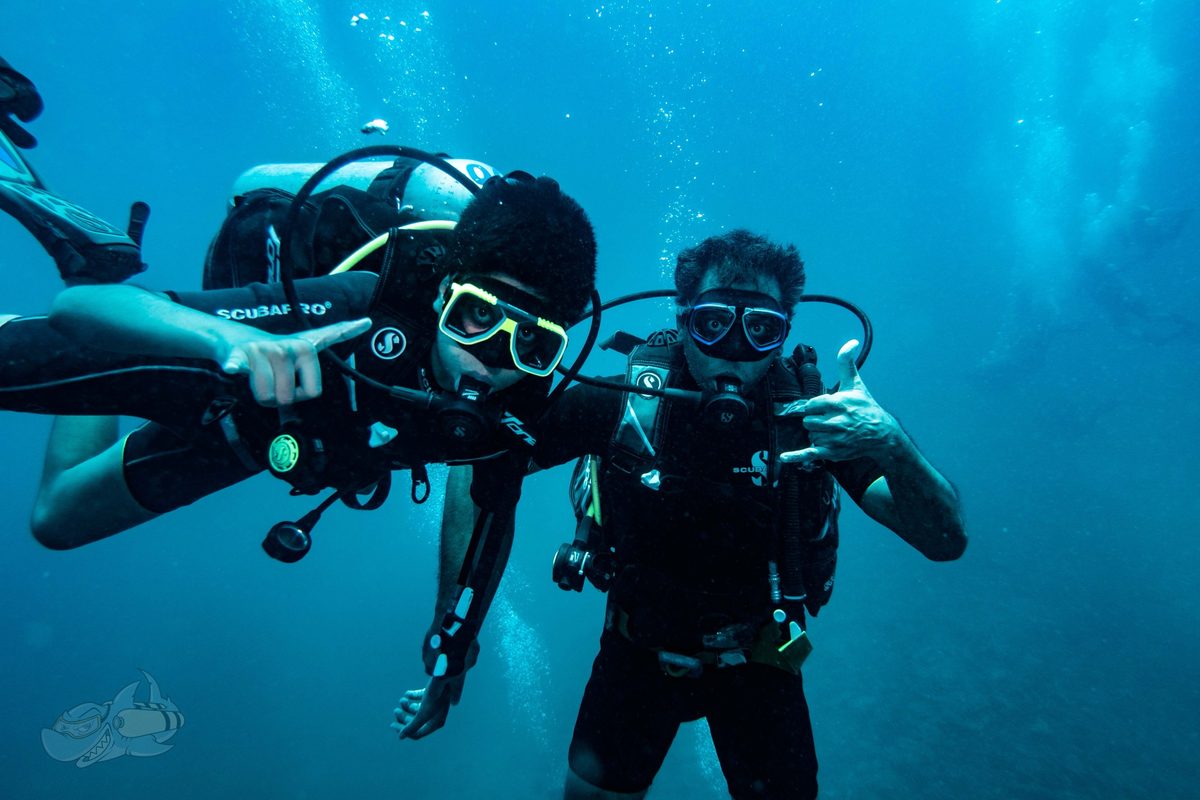 Buddy pair of divers side by side in blue water, facing the camera and signalling