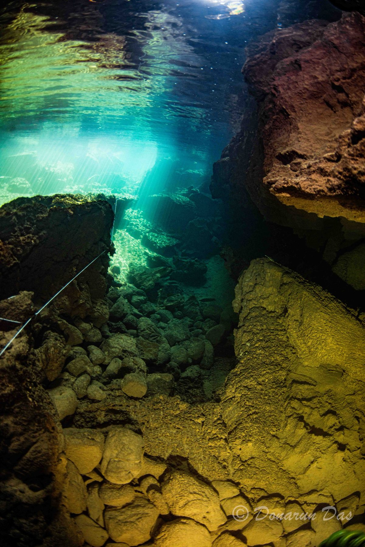 Sunbeams penetrating the surface into a rocky cavern with a guideline crossing the floor