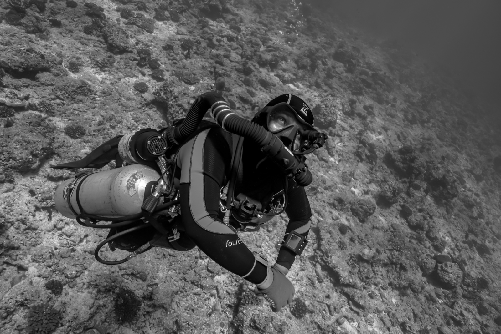 Black-and-white shot of a rebreather diver holding flat horizontal trim over a reef slope